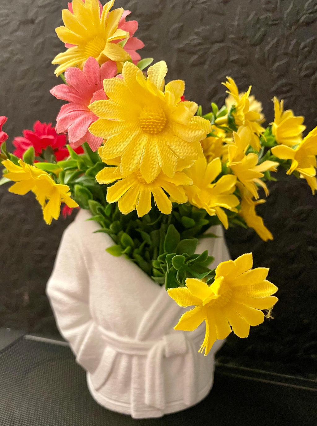 Bouquet of yellow and pink flowers in a white textured vase against a dark background